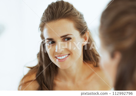 Happy young woman looking in mirror 112992796