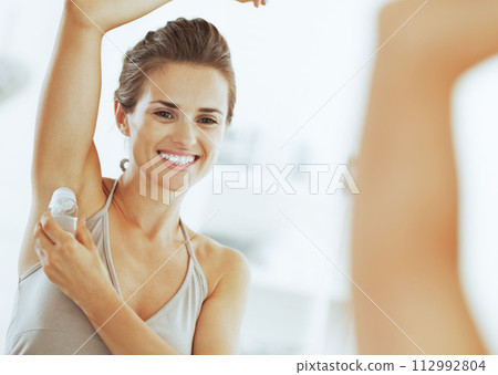 Smiling woman applying roller deodorant on underarm in bathroom Smiling woman applying roller deodorant on underarm in bathroom 112992804
