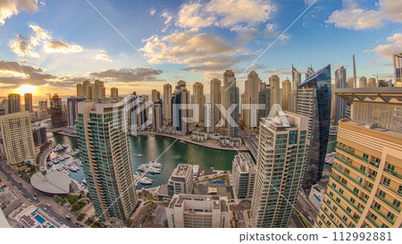 Modern skyscrapers and water channel with boats of Dubai Marina at sunset and day to night timelapse, United Arab Emirates. Modern skyscrapers and water channel with boats of Dubai Marina at sunset and day to night timelapse, United Arab Emirates. 112992881