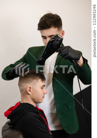 Haircut of a visitor in a barbershop. Hair styling with a comb and a hair dryer with hot air. Haircut of a visitor in a barbershop. Hair styling with a comb and a hair dryer with hot air. 112993248