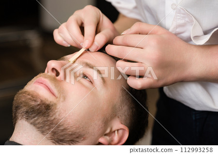 Hair removal procedure in a barbershop. Eyebrows hair wax removal. Hair removal procedure in a barbershop. Eyebrows hair wax removal. 112993258