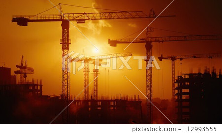 Construction cranes above the unfinished residential building against sunshine. Housing construction, apartment block in city Construction cranes above the unfinished residential building against sunshine. Housing construction, apartment block in city 112993555