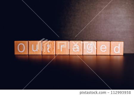 Wooden blocks form the text "Outraged" against a black background. Wooden blocks form the text "Outraged" against a black background. 112993938