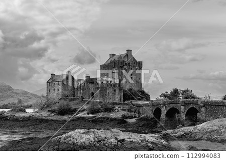 Grayscale showcase of Eilean Donan Castle timeless grandeur, with access bridge under a cloud sky Grayscale showcase of Eilean Donan Castle timeless grandeur, with access bridge under a cloud sky 112994083