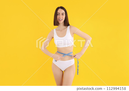A slim girl in underwear measures her waist. A slim girl in underwear measures her waist. 112994158