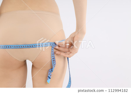 A slim girl in underwear measures the volume of her hips. A slim girl in underwear measures the volume of her hips. 112994182