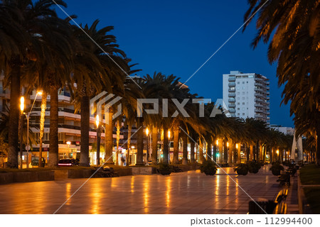 palm tree alley and sunset at beautiful Salou coastal town, tropical city street at evening, Tarragona province, Spain palm tree alley and sunset at beautiful Salou coastal town, tropical city street at evening, Tarragona province, Spain 112994400