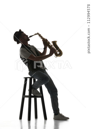 Talented young man making creative performance, playing saxophone isolate don white background. Black and white image. Talented young man making creative performance, playing saxophone isolate don white background. Black and white image. 112994578