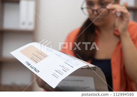 With a furrowed brow, woman pores over utility bills, mentally crunching numbers amidst mounting electricity, water, and internet bills With a furrowed brow, woman pores over utility bills, mentally crunching numbers amidst mounting electricity, water, and internet bills 112994580