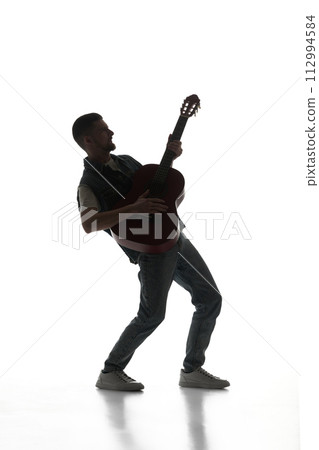 Artistic, talented young man playing guitar isolated on white background. Black and white image. 112994584