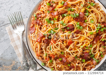 American spaghetti with bacon, minced meat, cheddar cheese and spicy tomato sauce close-up in a plate. Horizontal top view 112994714