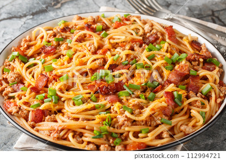 Delicious spaghetti with bacon, minced meat, cheddar cheese, onion and spicy tomato sauce close-up in a plate on the table. Horizontal 112994721