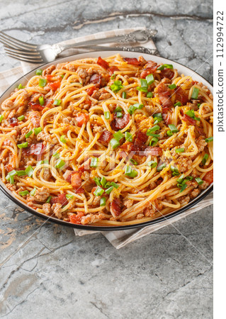 Western Cowboy Spaghetti with the addition of Ground beef, bacon, cheddar cheese, onion and hot sauce closeup on the plate. Vertical Western Cowboy Spaghetti with the addition of Ground beef, bacon, cheddar cheese, onion and hot sauce closeup on the plate. Vertical 112994722