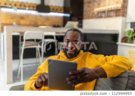 African american man in yellow hoodie with tablet in hands 112994993