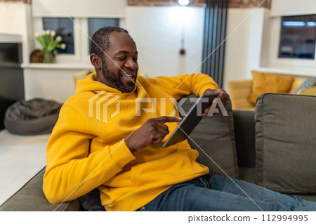African american man in yellow hoodie with tablet in hands 112994995