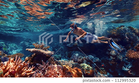attractive young man snorkels in the ocean and observes the coral world, free diver in the sea, coral reefs in the Maldives 112995320
