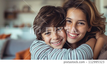 Portrait of beautiful young mother cuddling with teen son at home 112995323