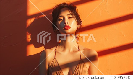 Portrait of beautiful woman with shadows of palm leaf or window blind on her face on warm background. Concept of sunbathing, vacation Portrait of beautiful woman with shadows of palm leaf or window blind on her face on warm background. Concept of sunbathing, vacation 112995798