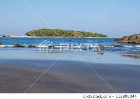 A god is enshrined on an island where shells have accumulated on a raised seabed under the blue sky, and around it are devil's washboards and eroded wavy rocks. 112996044