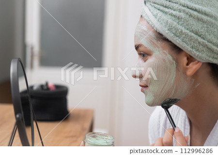 Skin's Delight: She graces her face with a moisturizing mask, nurturing her skin's health and beauty at home. Skin's Delight: She graces her face with a moisturizing mask, nurturing her skin's health and beauty at home. 112996286