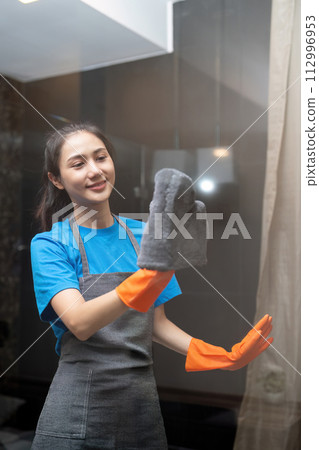 Asian woman cleaning the glass in the apartment. Cleaning staff maintain cleanliness in with towel and spray detergent 112996953