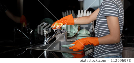 Woman washing up at home dishes in sink 112996978