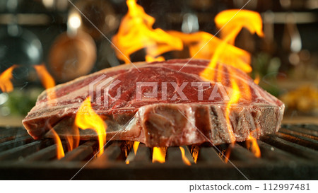 Close-up of tasty raw beef steak on cast-iron grate with fire flames 112997481