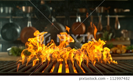Close-up of cast-iron grate with fire flames, dark background 112997482