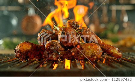 Close-up of tasty chicken legs on cast-iron grate with fire flames 112997483