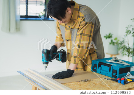 一個年輕人用電動螺絲起子工作 一個年輕人用電動螺絲起子工作 112999883