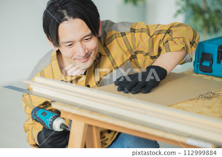 A young man working with an electric screwdriver A young man working with an electric screwdriver 112999884