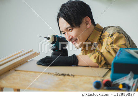 一個年輕人用電動螺絲起子工作 一個年輕人用電動螺絲起子工作 112999887