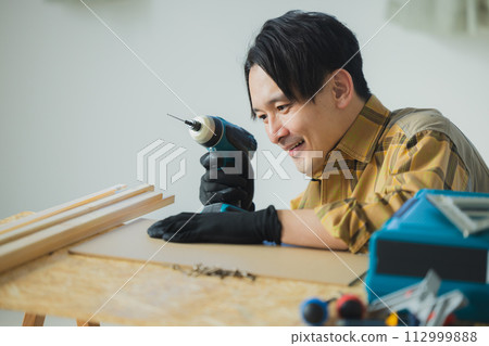 一個年輕人用電動螺絲起子工作 112999888