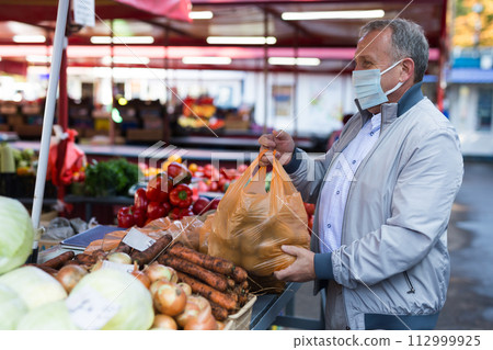 Man in face mask purchasing potatoes in greengrocery Man in face mask purchasing potatoes in greengrocery 112999925