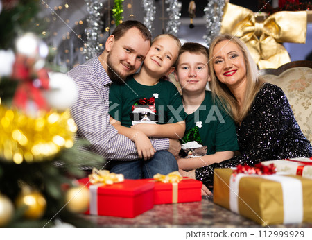 Portrait of happy family with two children celebrating Christmas next to Christmas tree Portrait of happy family with two children celebrating Christmas next to Christmas tree 112999929