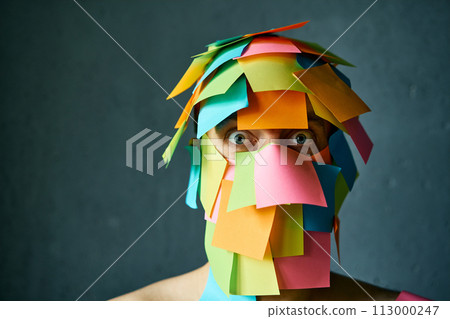 Close up portrait of shocked man with colorful sticky notes all over his face over gray background 113000247