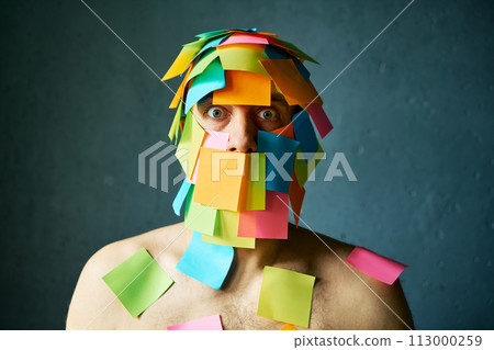 Shocked amazed man with colorful sticky notes all over his face over gray background 113000259