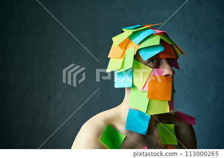 Close up portrait of man covered with colorful sticky notes all over his face and body looking to camera Close up portrait of man covered with colorful sticky notes all over his face and body looking to camera 113000265