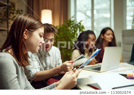 University students sitting together at table with books and laptops, studying together, doing projects 113002874
