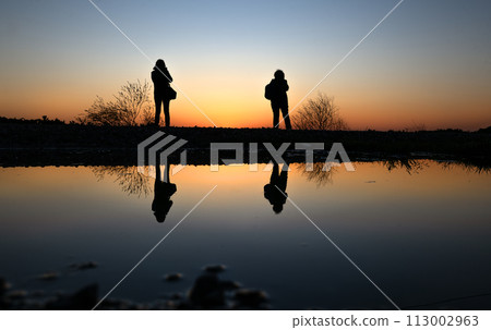 Reflections in the water of silhouette female photographers taking sunrise photos 113002963