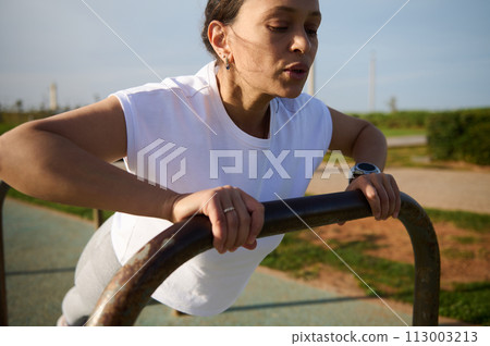 Sporty young woman in sportswear doing bar push-ups, exercising outdoors in the urban sportsground 113003213