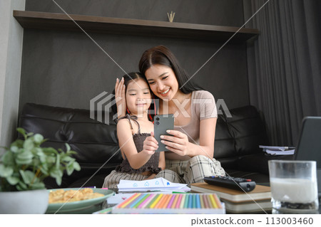 Beautiful Asian mother working at home and taking care of cute little daughter Beautiful Asian mother working at home and taking care of cute little daughter 113003460