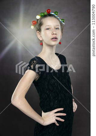 A funny teenager girl with a wreath of sweets on her head is shot against a gray background with a beam from a spotlight. A funny teenager girl with a wreath of sweets on her head is shot against a gray background with a beam from a spotlight. 113004790