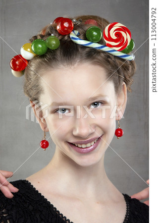 Portrait of a funny teenage girl with a wreath of sweets on her head. Portrait of a funny teenage girl with a wreath of sweets on her head. 113004792