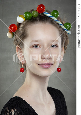 Portrait of a funny teenage girl with a wreath of sweets on her head. Portrait of a funny teenage girl with a wreath of sweets on her head. 113004794
