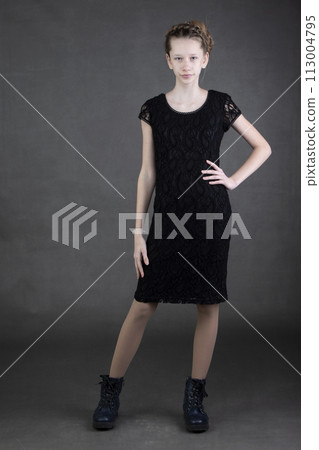 A beautiful thin teenage girl in a black dress and boots is shot on a gray background. A beautiful thin teenage girl in a black dress and boots is shot on a gray background. 113004795