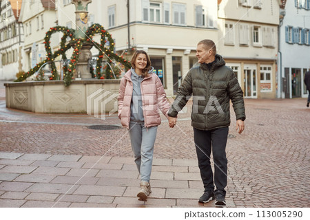 Loving couple of tourists walking around old town. Couple of lovers leisurely stroll in the cool autumn morning on the streets of a BIETIGHEIM-BISSINGEN (Germany). The guy holds his wife. Vacation Loving couple of tourists walking around old town. Couple of lovers leisurely stroll in the cool autumn morning on the streets of a BIETIGHEIM-BISSINGEN (Germany). The guy holds his wife. Vacation 113005290