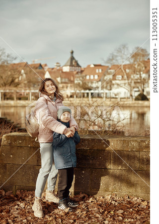 Riverside Family Harmony: Mother, 30 Years Old, and Son - Beautiful 8-Year-Old Boy, Standing by Neckar River and Historic Half-Timbered Town, Bietigheim-Bissingen, Germany, Autumn 113005351