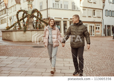 Loving couple of tourists walking around old town. Couple of lovers leisurely stroll in the cool autumn morning on the streets of a BIETIGHEIM-BISSINGEN (Germany). The guy holds his wife. Vacation Loving couple of tourists walking around old town. Couple of lovers leisurely stroll in the cool autumn morning on the streets of a BIETIGHEIM-BISSINGEN (Germany). The guy holds his wife. Vacation 113005356