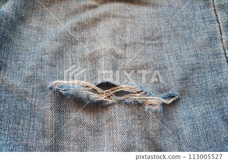 A worn-out torn leg of jeans with white fibers coming out. The concept of obsolescence and depreciation 113005527